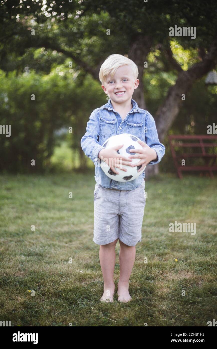 Ritratto del ragazzo carino in piedi mentre tiene il calcio in cortile Foto Stock