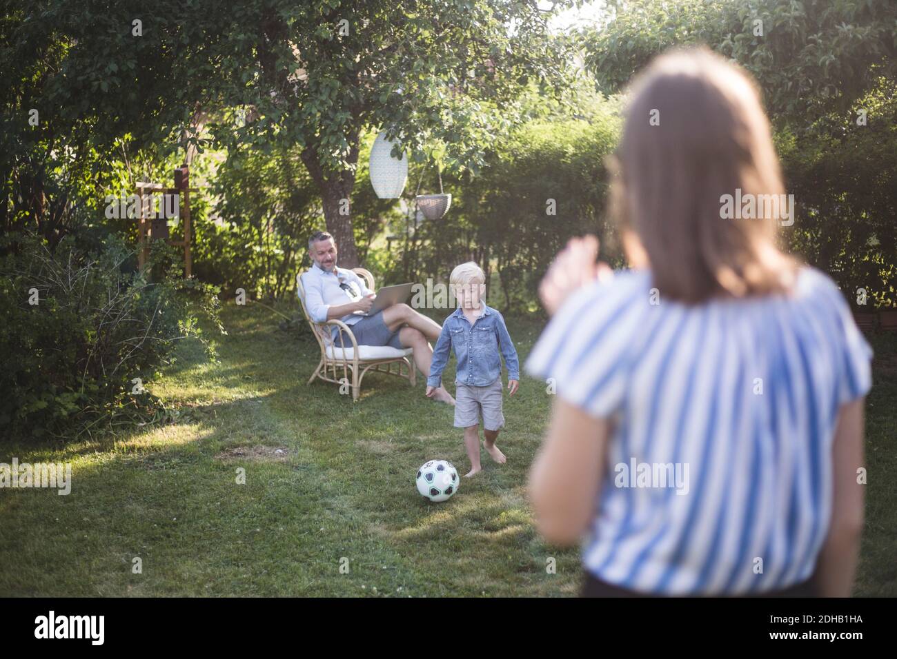 Padre che guarda il figlio che gioca a calcio con la figlia alla schiena iarda Foto Stock