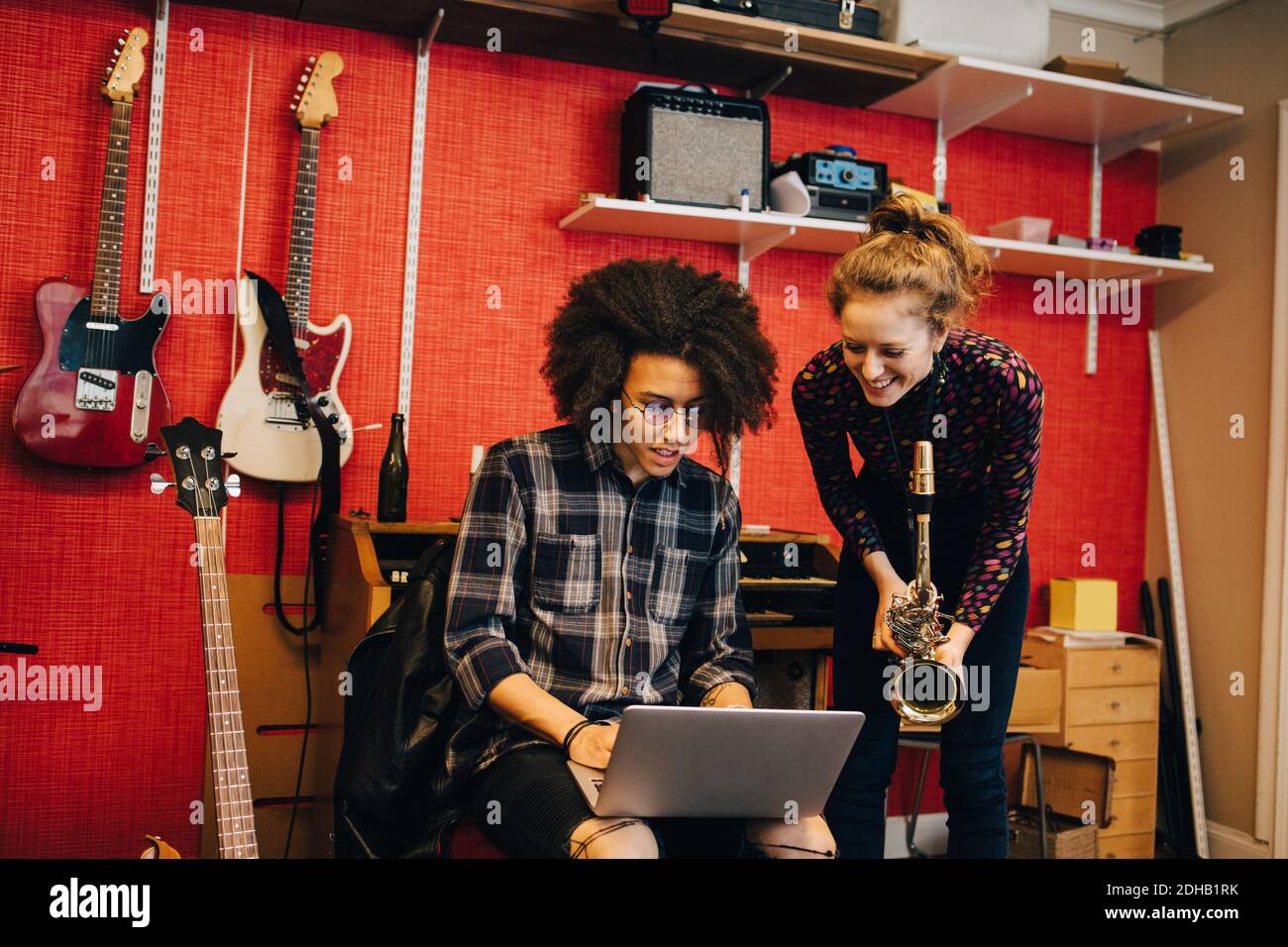 Donna con sassofono che guarda l'uomo usando il laptop mentre si pratica in studio di registrazione Foto Stock