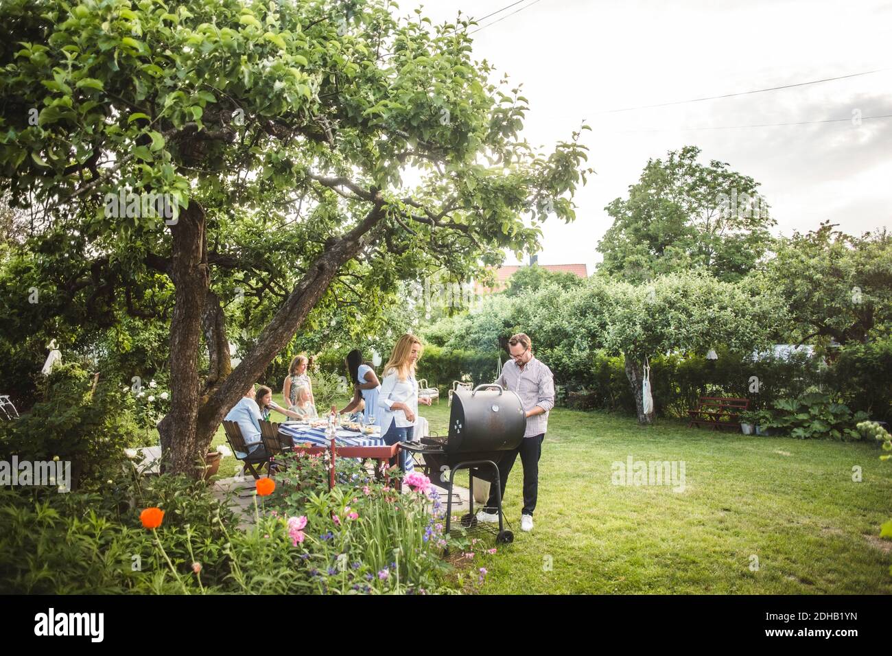 Amici maschili e femminili che preparano il cibo sul barbecue mentre la famiglia divertirsi in cortile Foto Stock