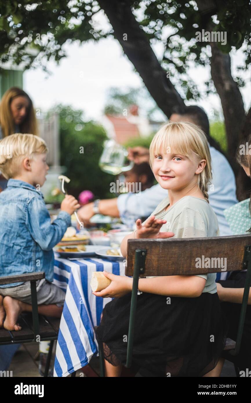 Ritratto di sorridente ragazza seduta con amici e famiglia a. tavolo in festa in giardino Foto Stock