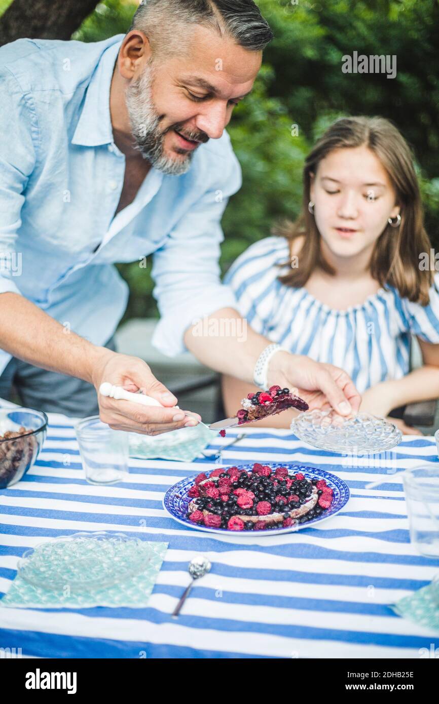 Uomo che serve crostata di bacche a figlia a tavola in cortile Foto Stock