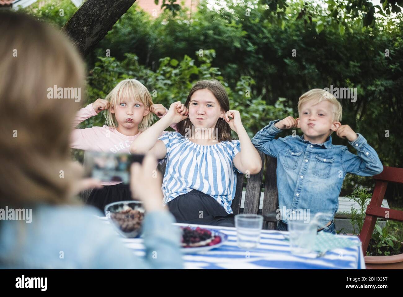 Donna che fotografa i bambini mentre fa i volti al tavolo da pranzo dentro festa in giardino Foto Stock