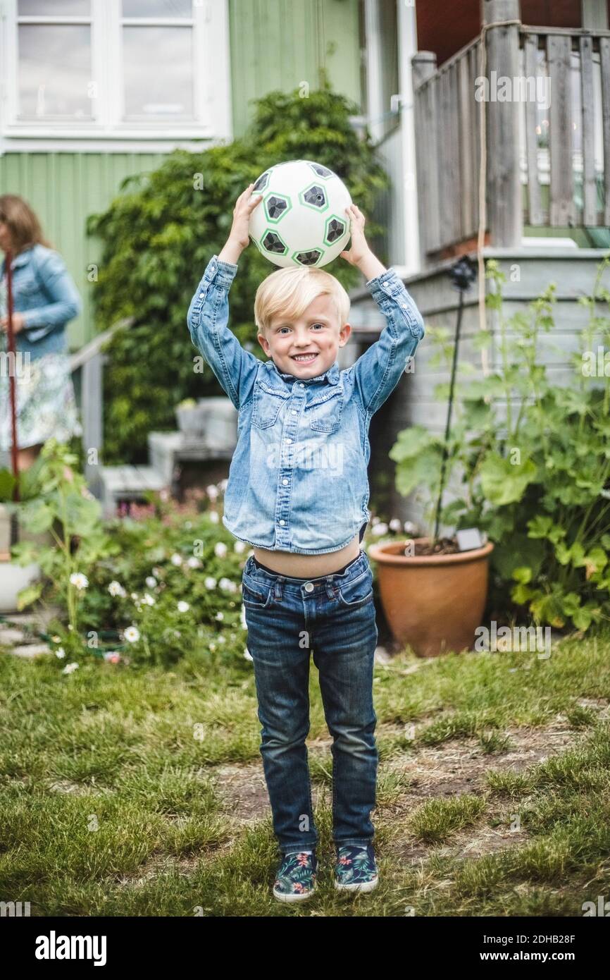 Tutta la lunghezza del ragazzo sorridente che tiene la palla di calcio sulla testa in piedi in giardino Foto Stock