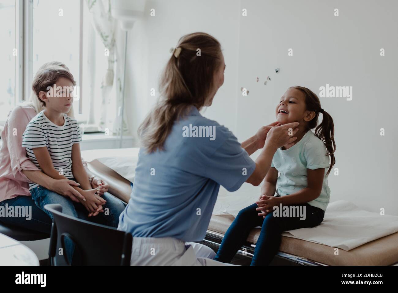 Donna medico che esamina la ragazza sorridente mentre la famiglia si siede in medicina camera Foto Stock