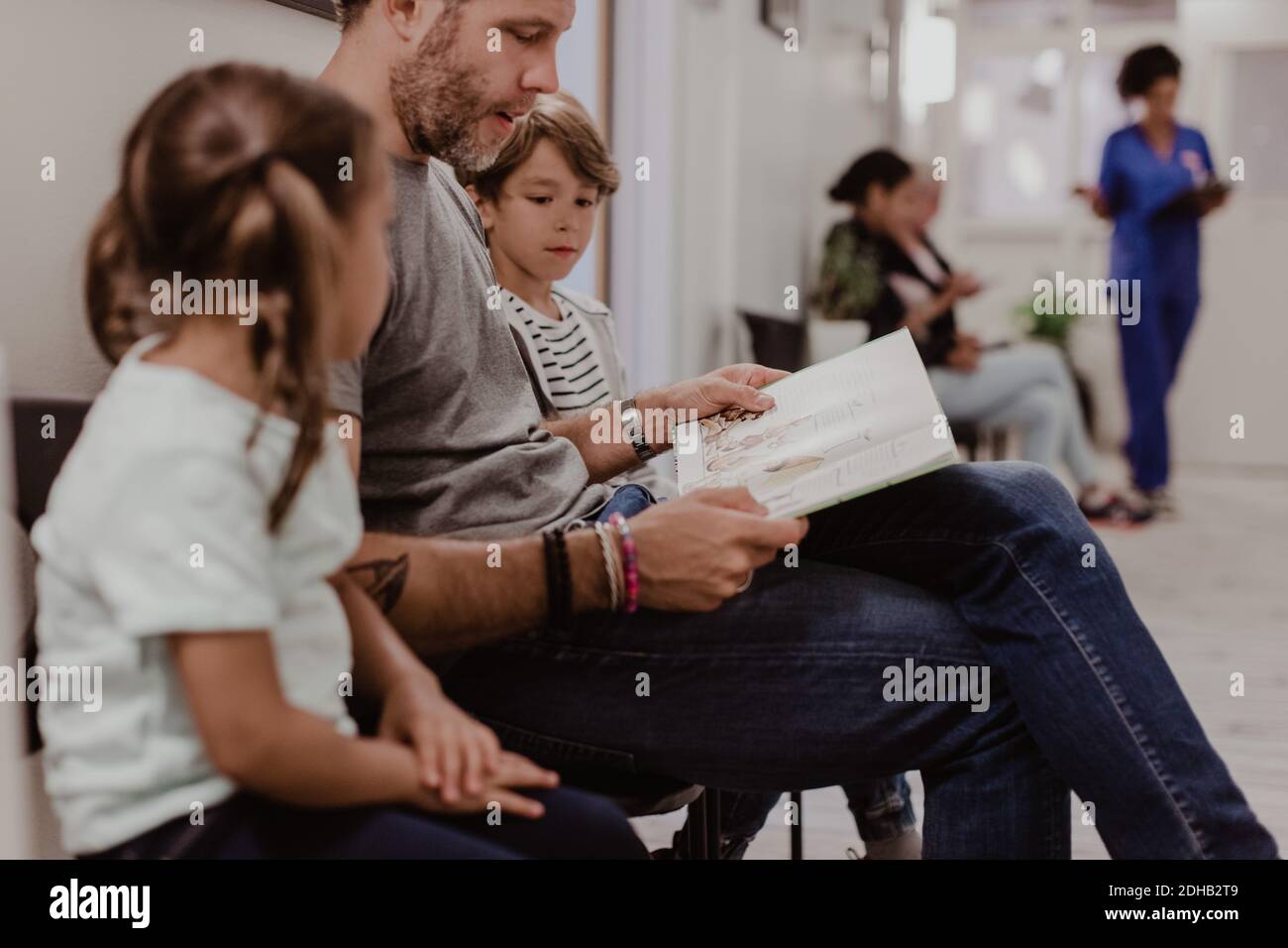 Padre leggere libro per figlio e figlia mentre si aspetta corridoio ospedaliero Foto Stock