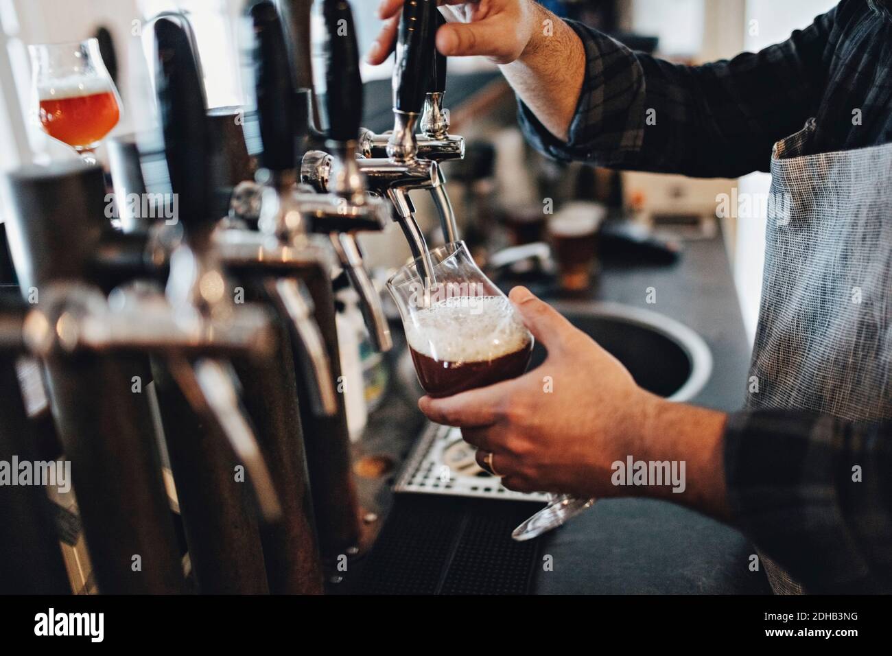 Sezione centrale del bicchiere di riempimento del barman mentre si utilizza il rubinetto della birra su ristorante Foto Stock