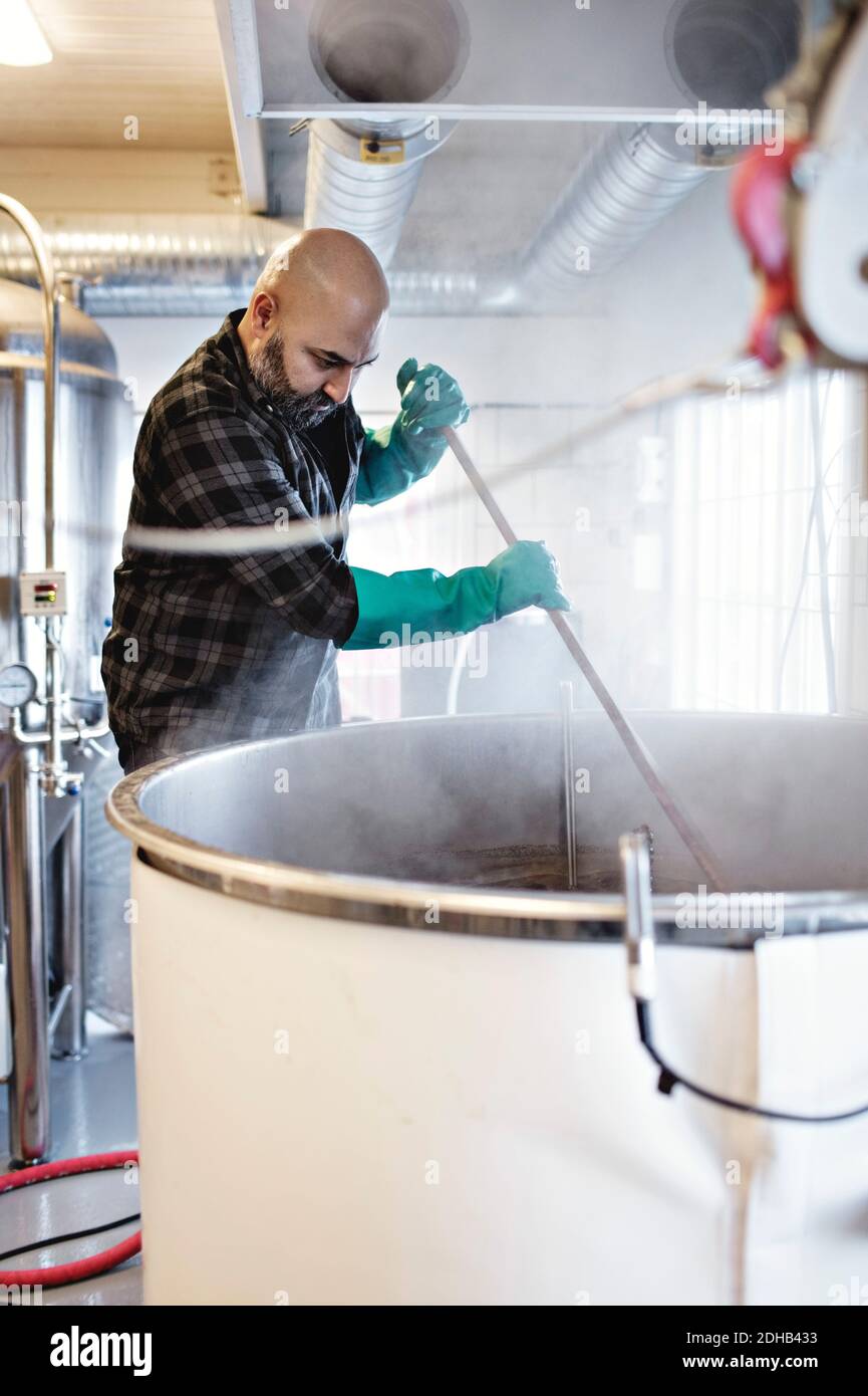Lavoratore maschile mescolando la birra nel contenitore mentre lavora alla fabbrica di birra Foto Stock