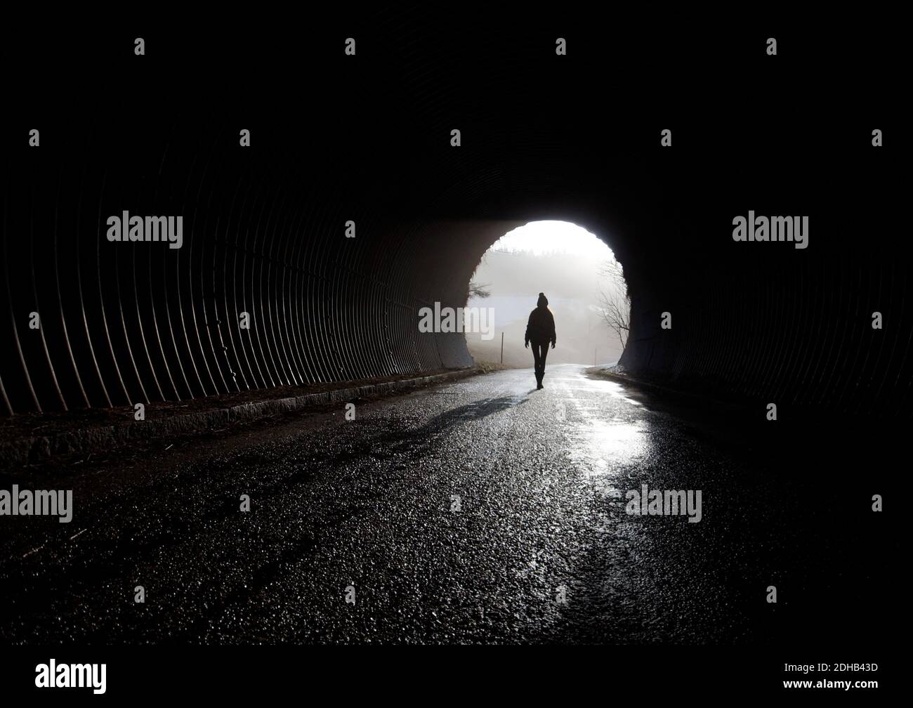 luce alla fine del tunnel, silhouette che cammina attraverso le tenebre Foto Stock