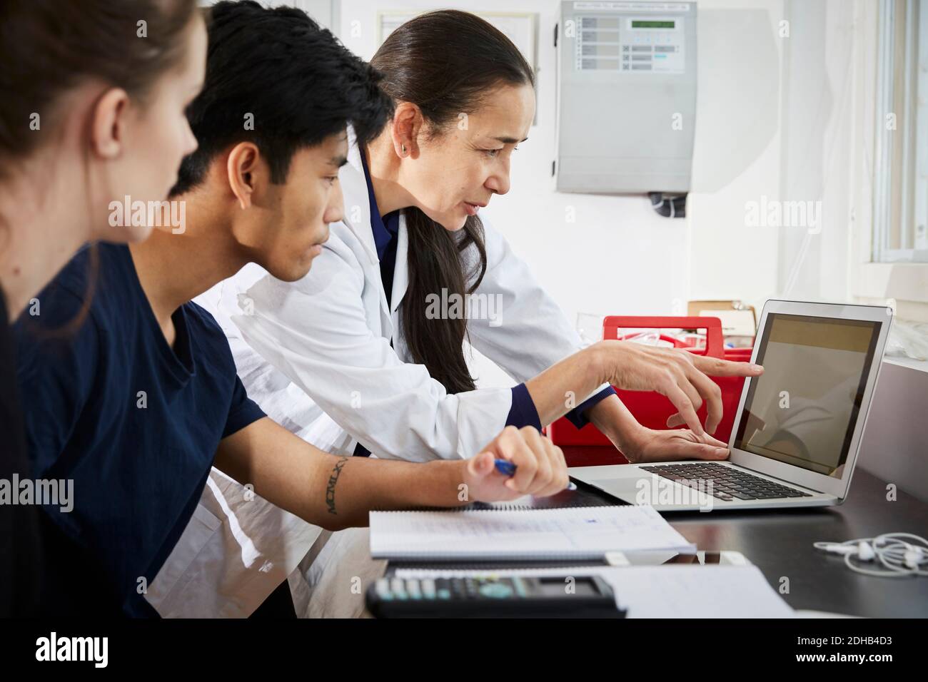 Insegnante che indica lo schermo del laptop ai giovani studenti di ingegneria in aula Foto Stock
