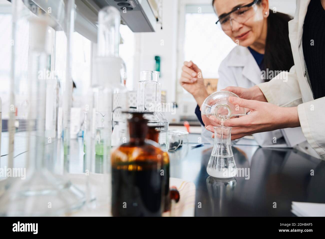 La sezione intermedia della soluzione di versamento della giovane studentessa in fiasca da insegnante presso il laboratorio di chimica Foto Stock