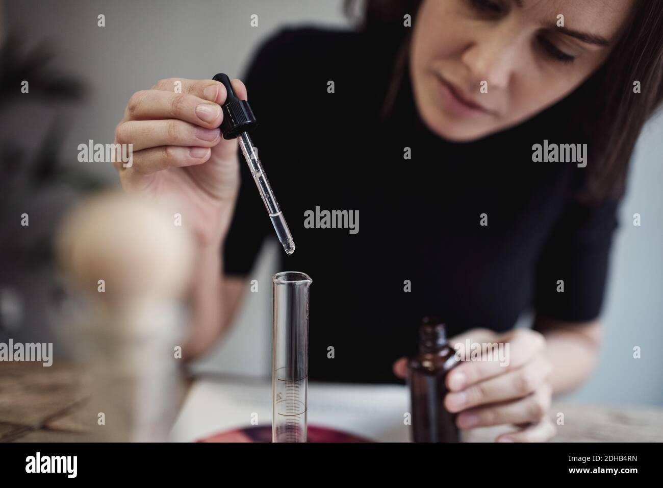 Donna che utilizza una pipetta per miscelare il liquido dal flacone seduto a tavola in laboratorio di profumi Foto Stock