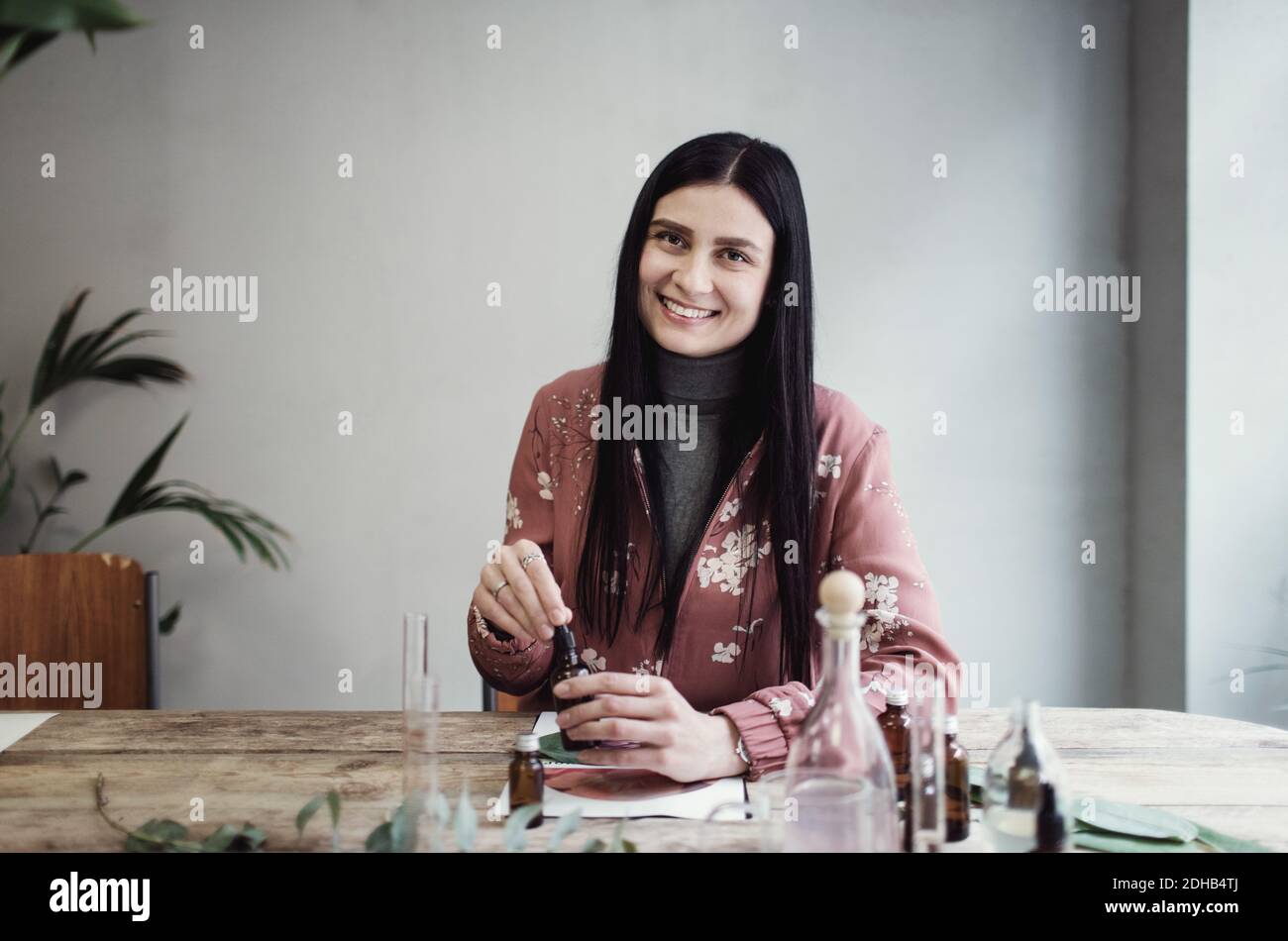 Ritratto di sorridente imprenditore femminile che prepara profumo a tavola in officina Foto Stock