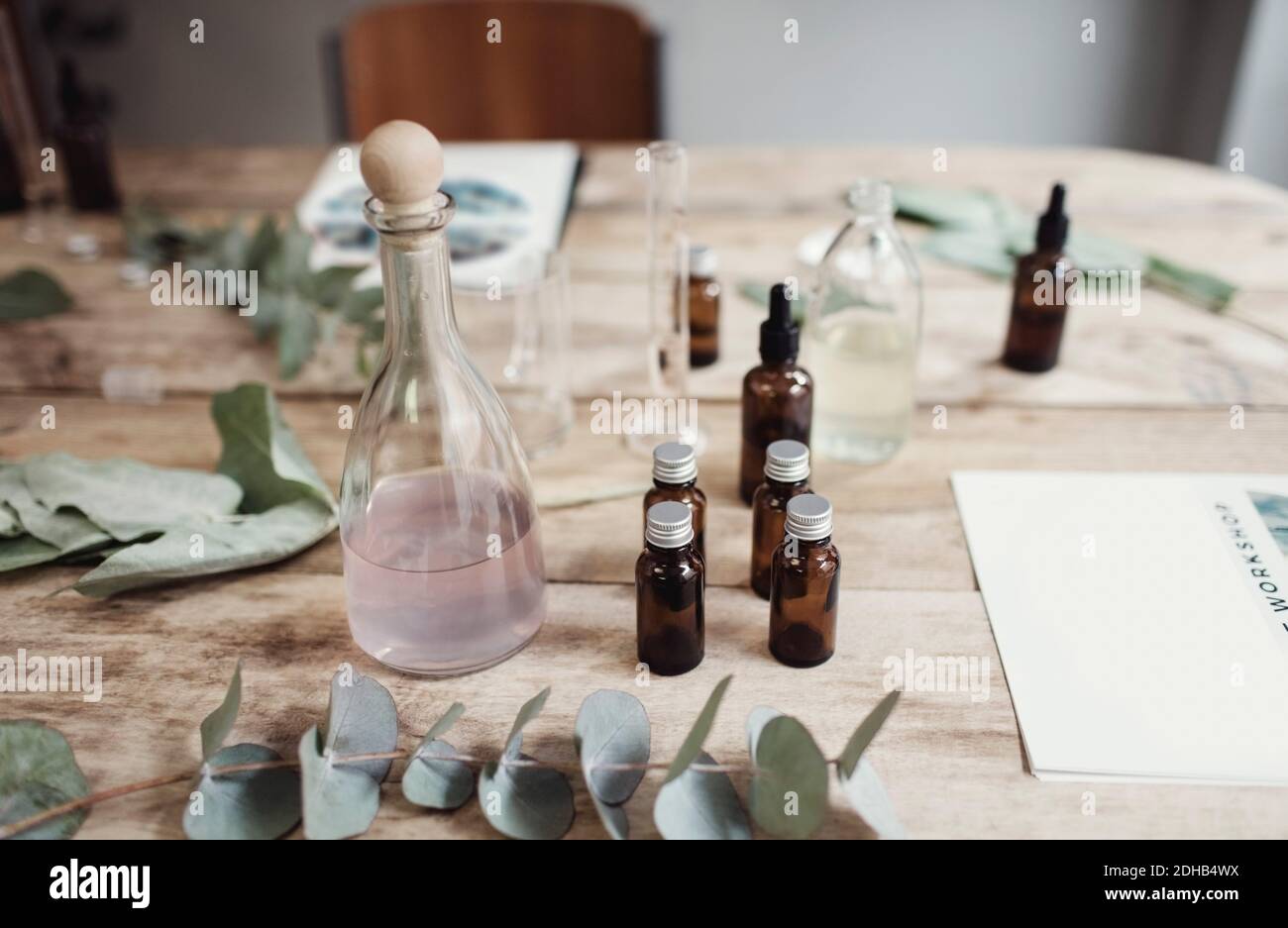 Vista ad alto angolo di varie bottiglie di profumo tra foglie e. opuscoli sul tavolo in officina Foto Stock