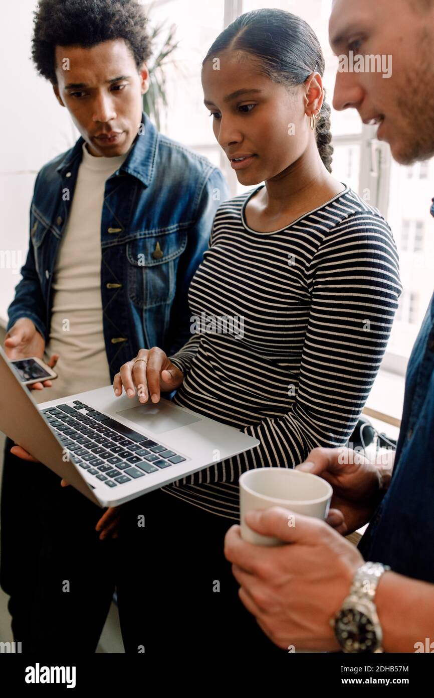 Giovane imprenditore femminile che tiene il laptop mentre discute con i dirigenti dentro ufficio Foto Stock