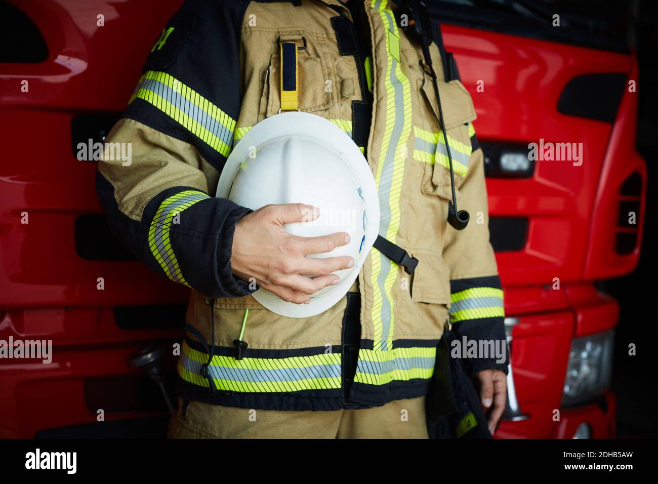 Sezione centrale del pompiere femminile che tiene il casco mentre si è in piedi al fuoco stazione Foto Stock