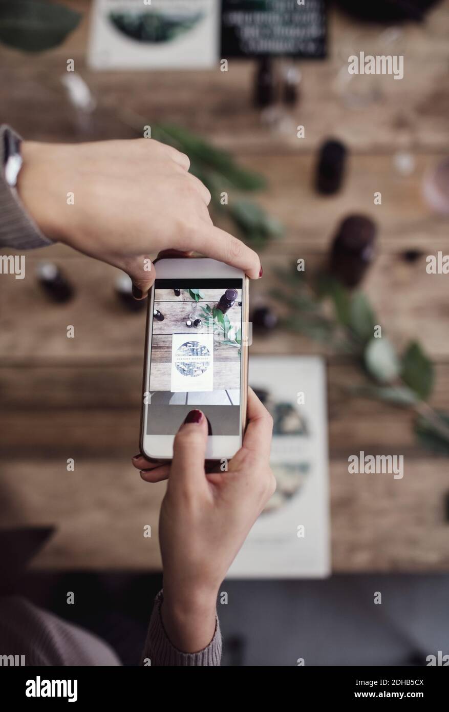 Mani tagliate di donna che fotografa la brochure sul tavolo al profumo officina Foto Stock Mani tagliate di donna che fotografa la brochure sul tavolo al profumo officina Foto Stock