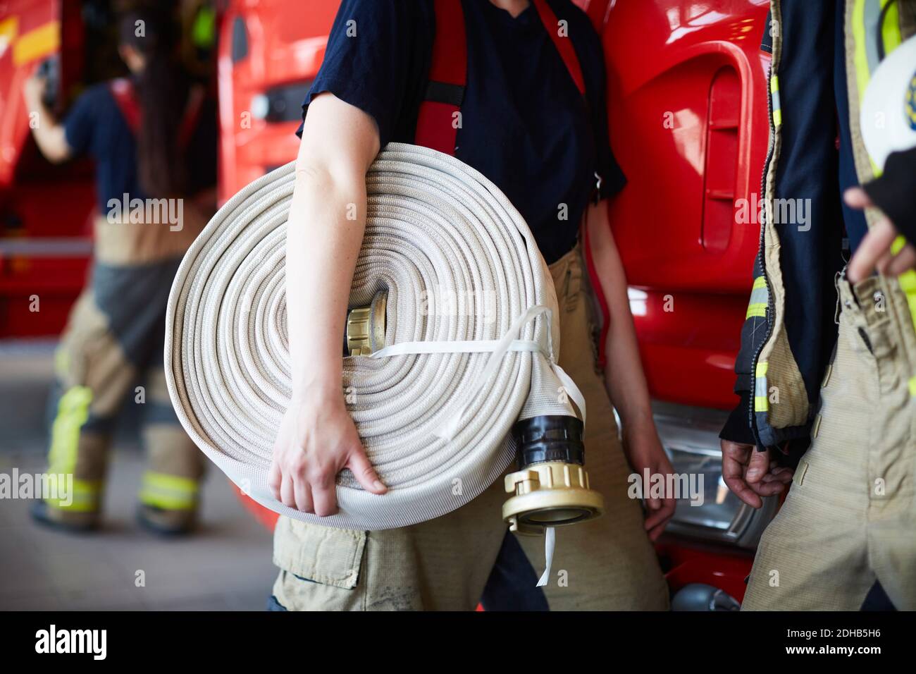 Sezione centrale del pompiere femmina che tiene arrotolato il tubo flessibile del fuoco mentre in piedi con il collaboratore alla stazione dei vigili del fuoco Foto Stock