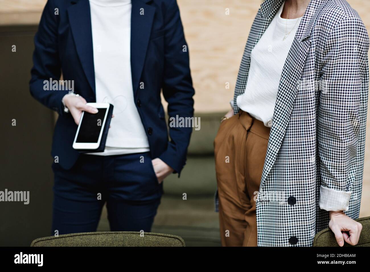 La sezione centrale di businesswoman che tiene il telefono mobile mentre sta in piedi con la femmina professionale in ufficio Foto Stock