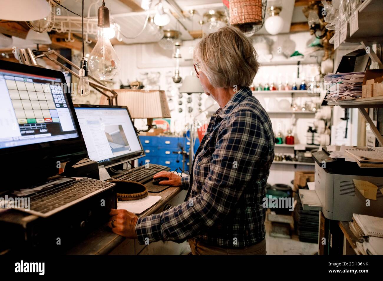 Vista laterale di un venditore senior che utilizza il computer mentre si sta in piedi checkout in negozio di hardware Foto Stock