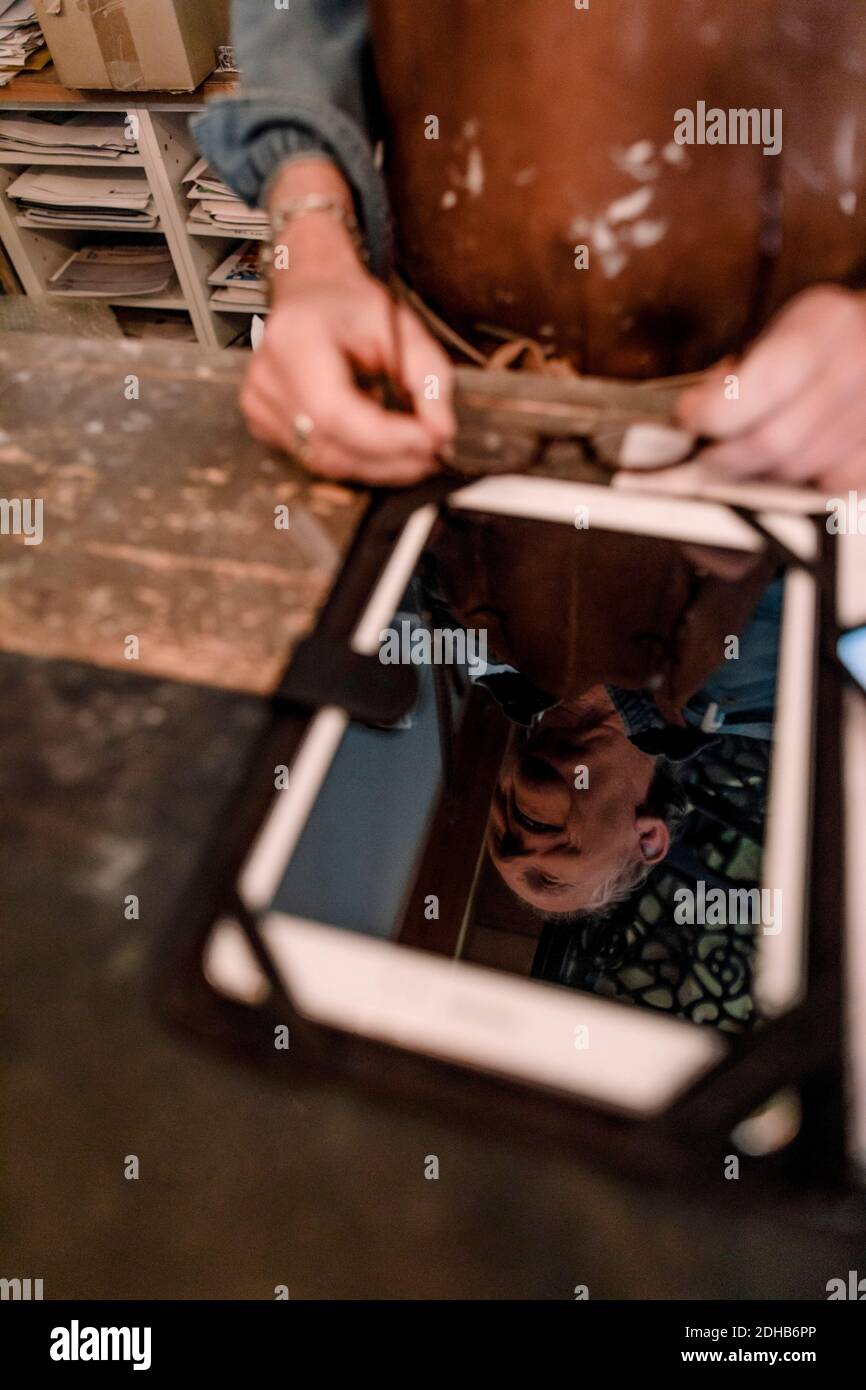 Visualizzazione ad alto angolo di un venditore senior che riflette su un tablet digitale schermo al banco di cassa nel negozio di hardware Foto Stock