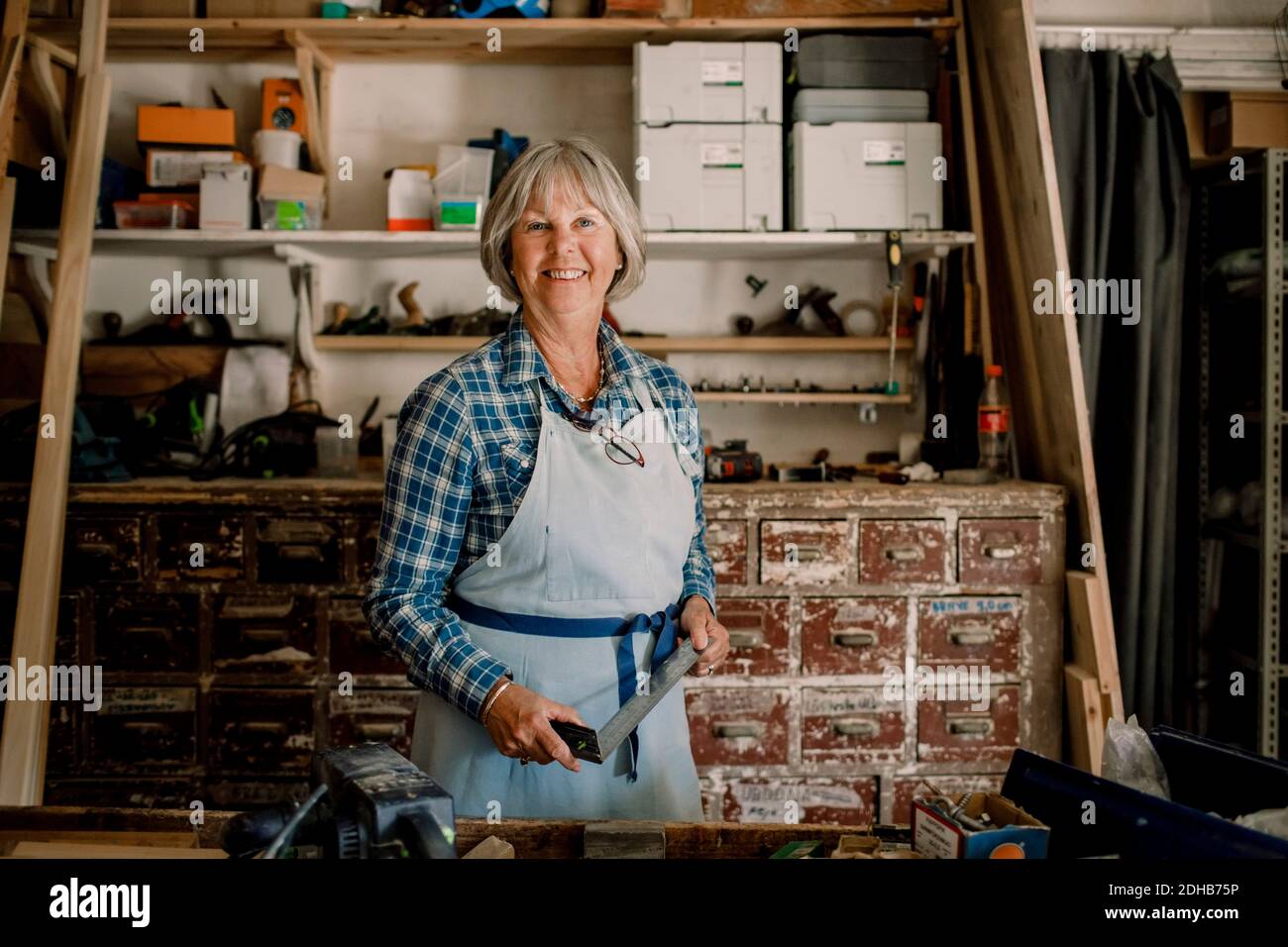 Ritratto dell'imprenditore femminile sicuro che tiene il quadrato fissato a. officina Foto Stock