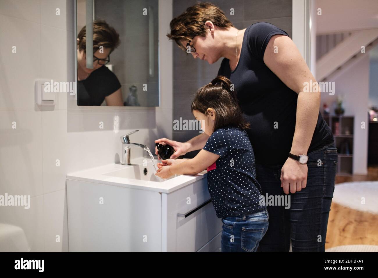 Donna che assiste la figlia nel lavarsi le mani al lavello in casa Foto Stock