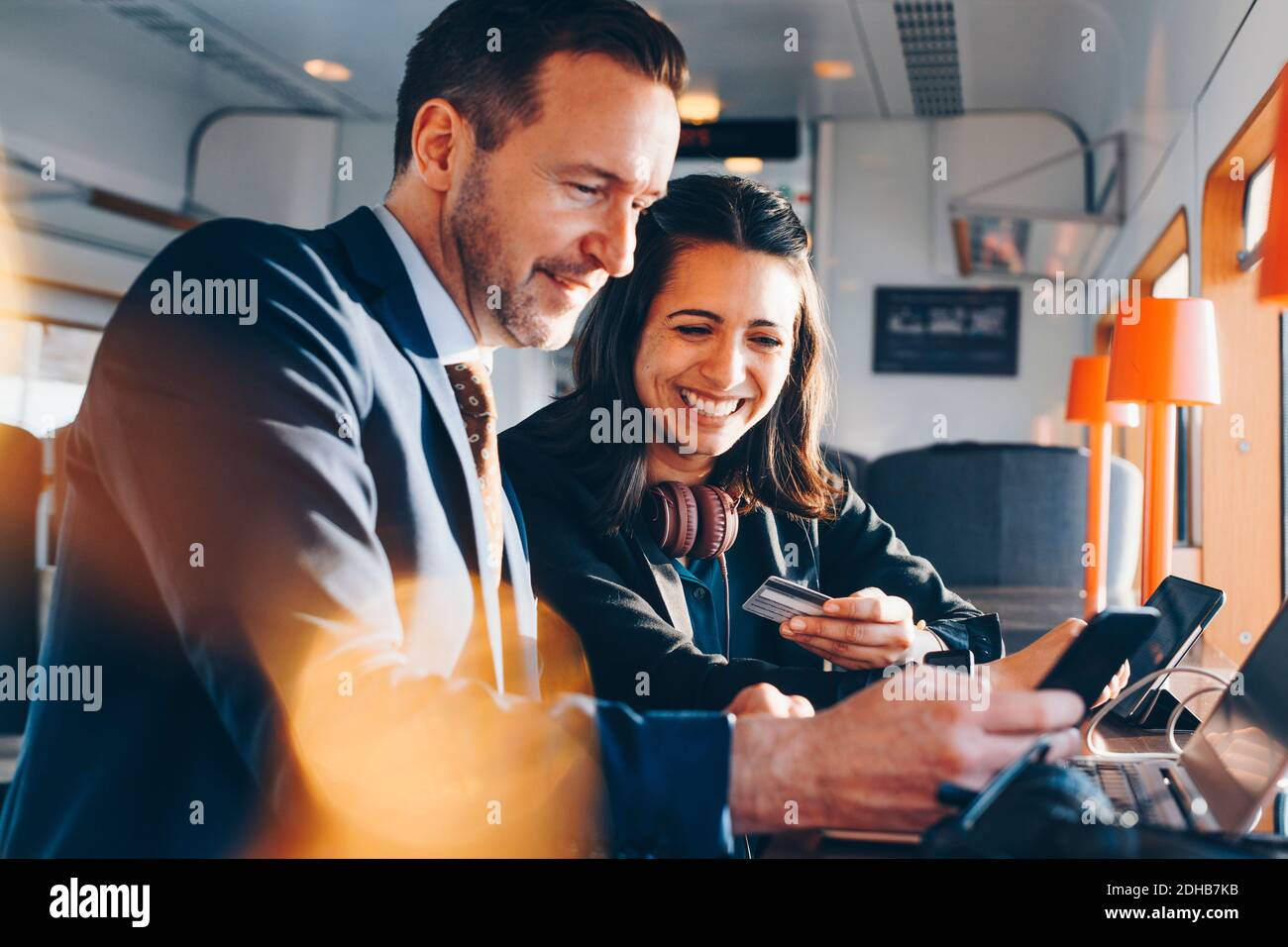 Donna d'affari felice che tiene la carta di credito mentre l'uomo d'affari usa il telefono mobile presso la lobby dell'aeroporto Foto Stock