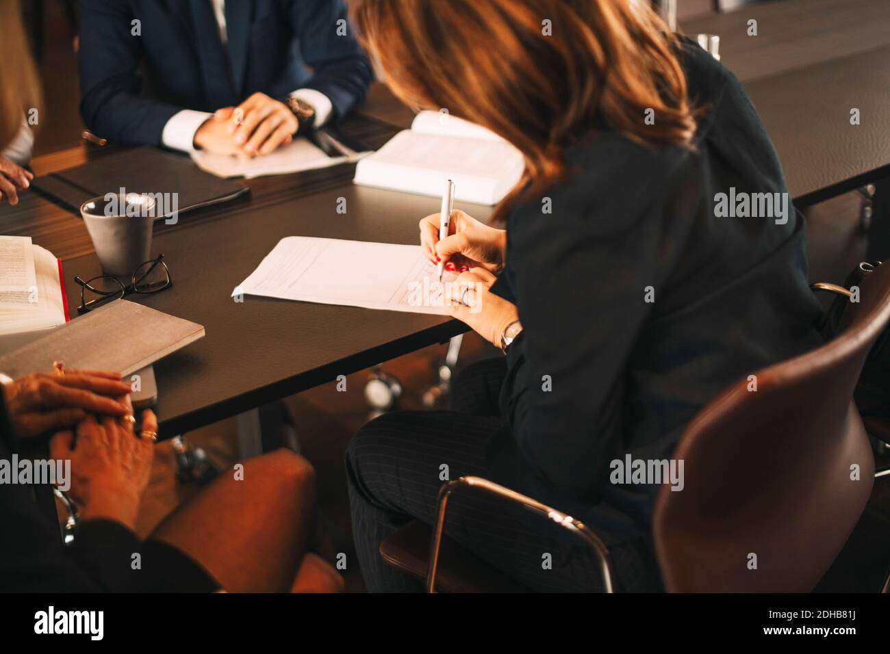 Avvocato donna che firma documenti mentre siede in riunione con i colleghi in ufficio Foto Stock