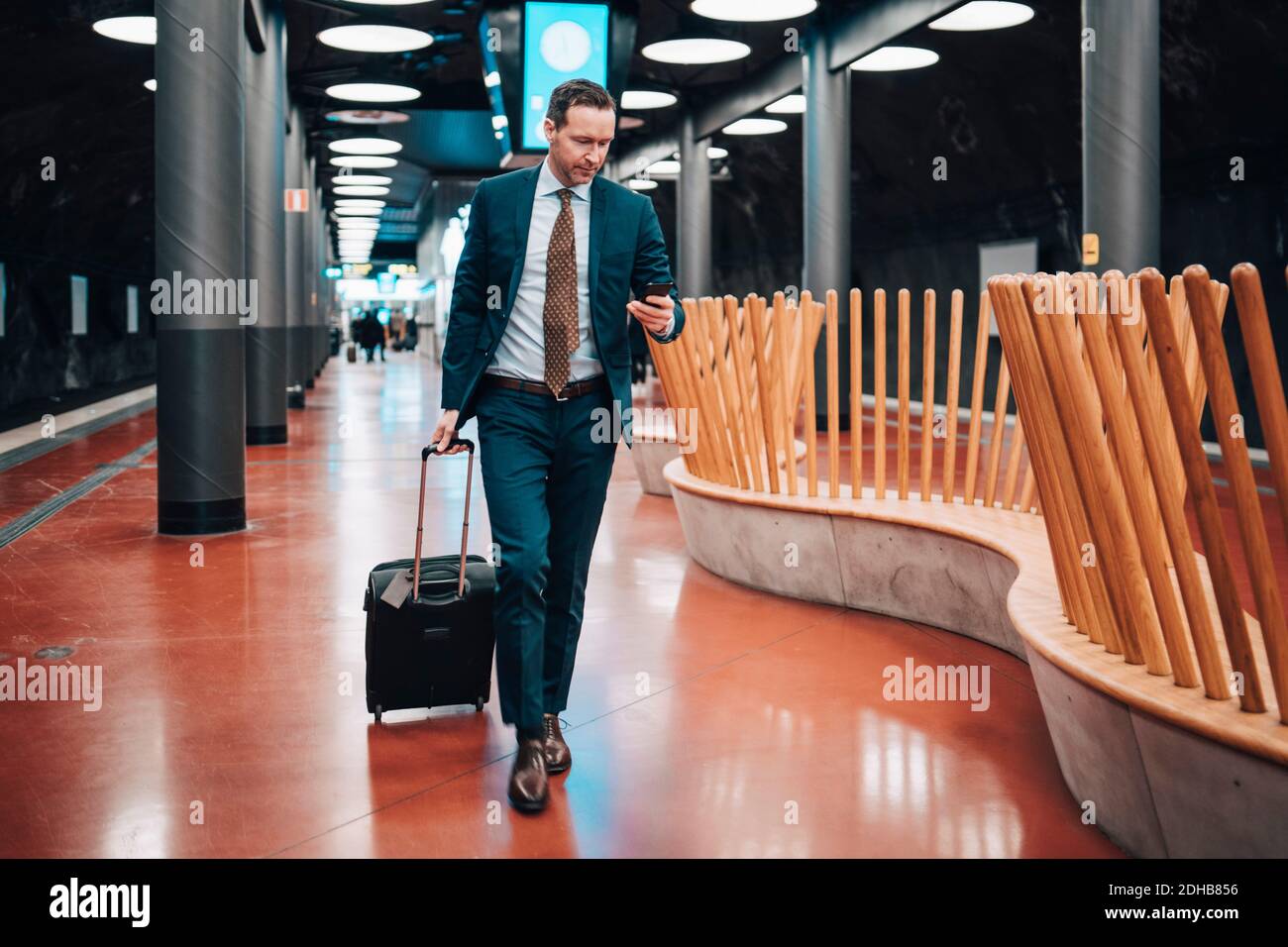 Lunghezza completa di uomo d'affari con bagagli e telefono cellulare a piedi nella piattaforma ferroviaria Foto Stock