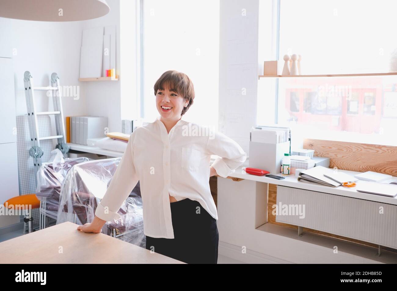 Donna sorridente professionista di design in piedi alla scrivania in officina Foto Stock