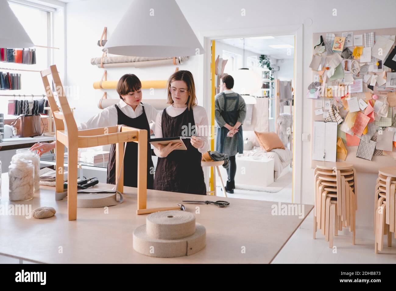 Le donne che lavorano nella tappezzeria leggono l'imbottitura con la sedia sulla scrivania in officina Foto Stock