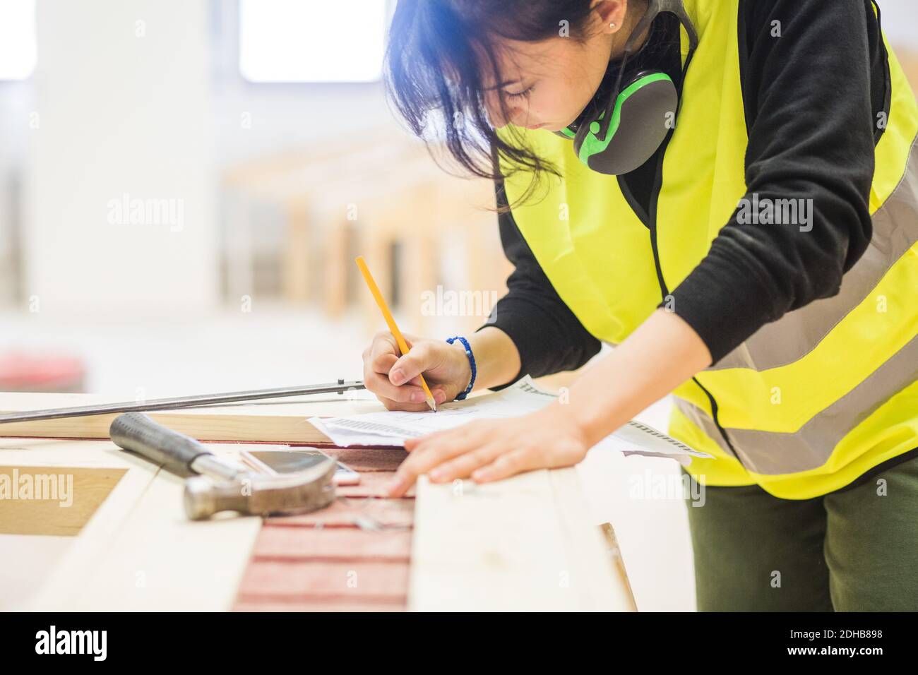 Giovane tirocinante femminile che si disegna su carta al banco di lavoro in illuminato officina Foto Stock