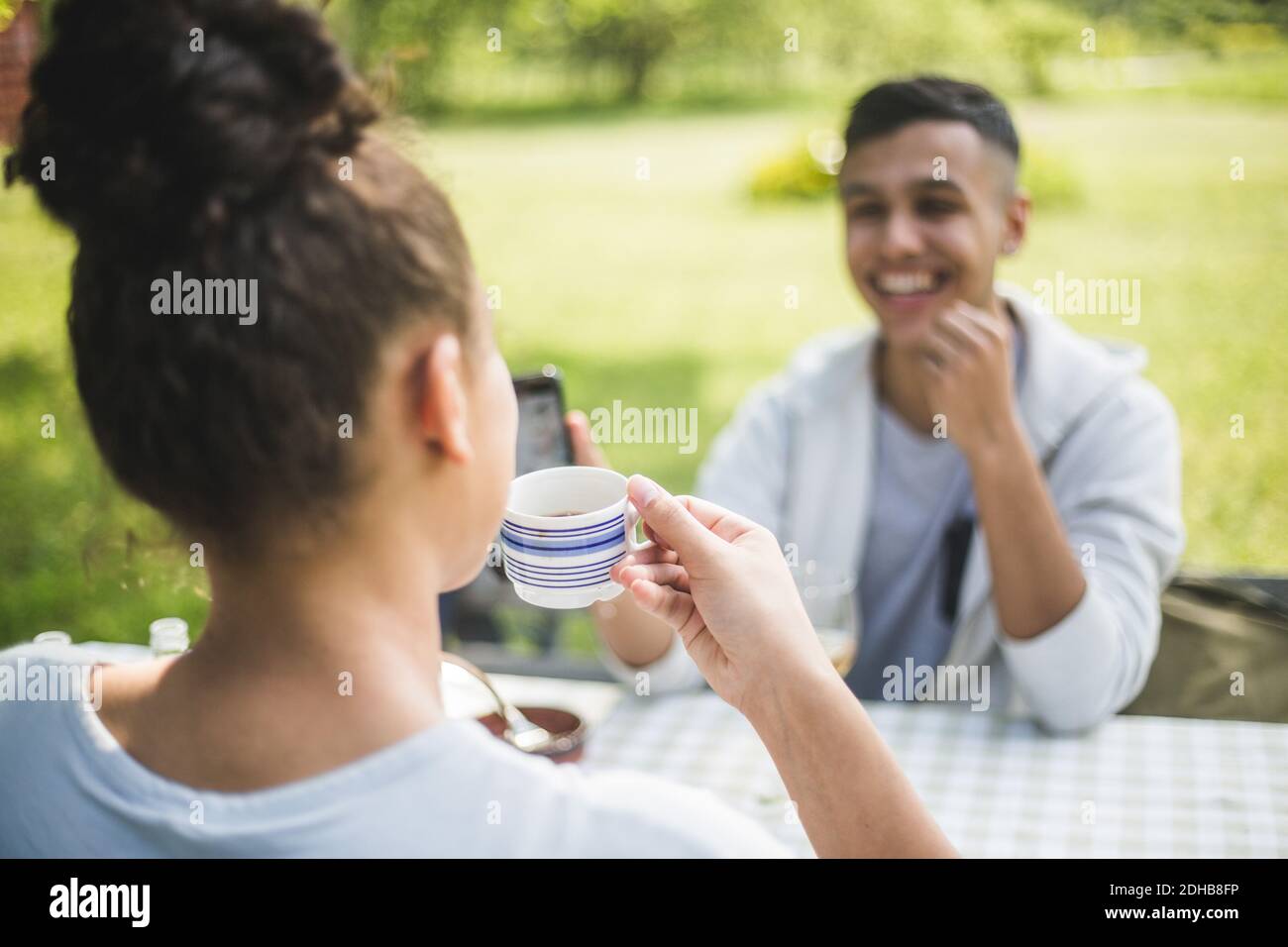 Ragazzo sorridente che guarda l'amico femmina che beve il caffè dentro ristorante Foto Stock