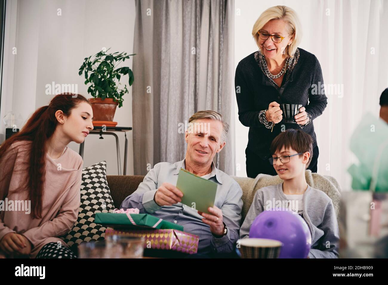 Nonno con compleanno presenta lettura biglietto d'auguri per la famiglia in soggiorno Foto Stock