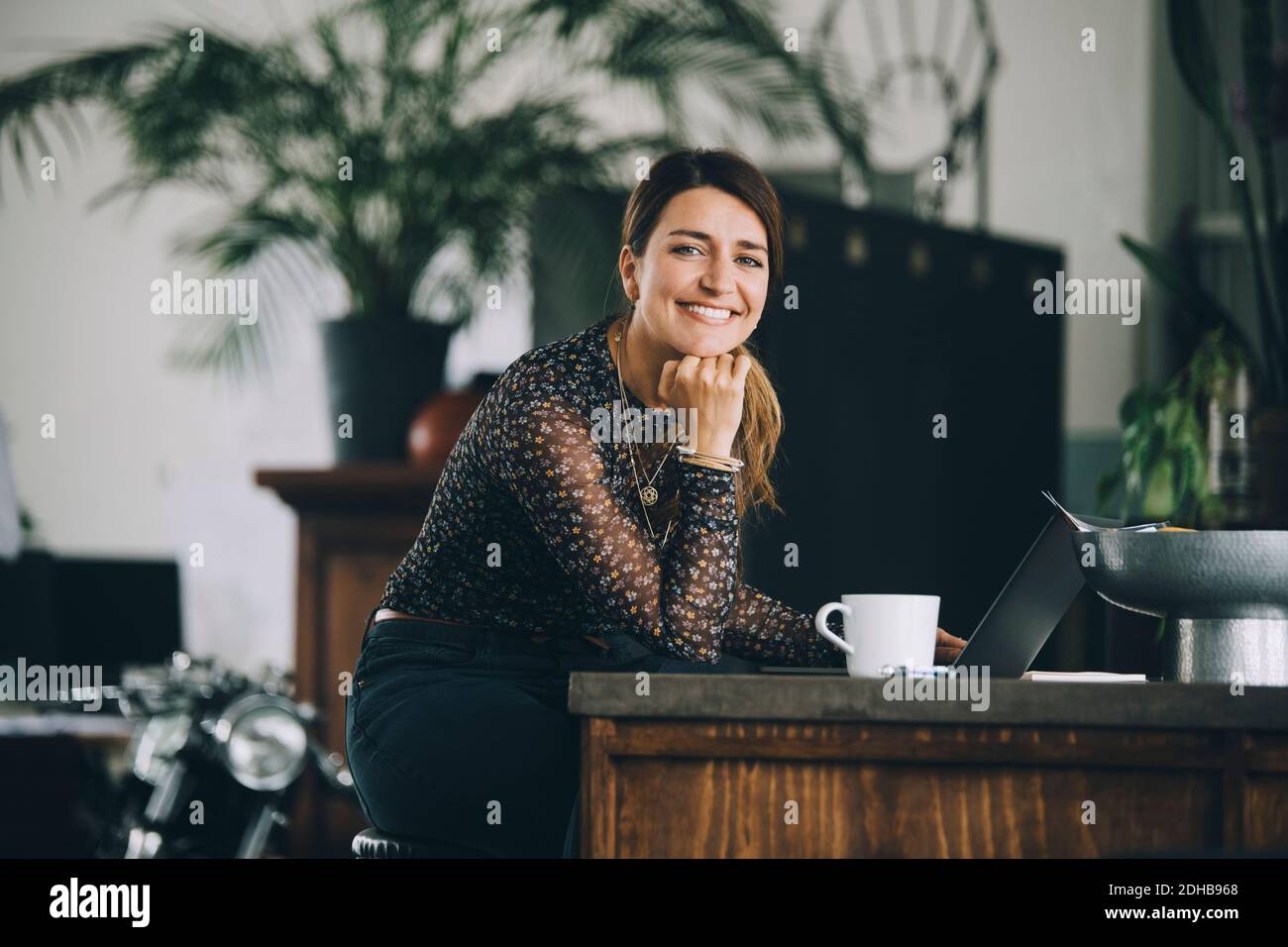 Ritratto di donna d'affari sorridente con la mano sul mento seduto a. isola cucina in ufficio creativo Foto Stock