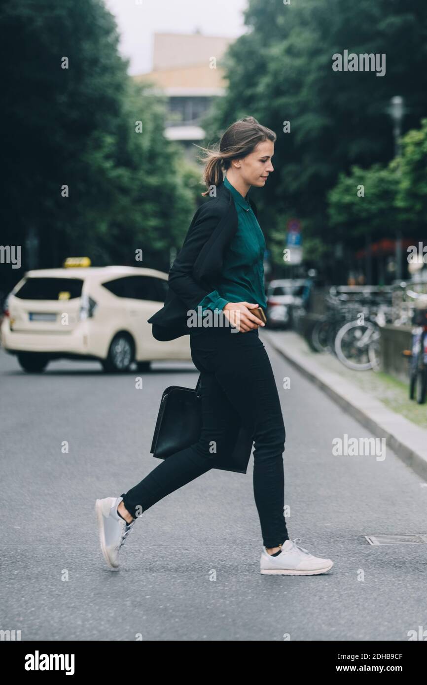 Vista laterale di una donna d'affari creativa che attraversa la strada in città Foto Stock