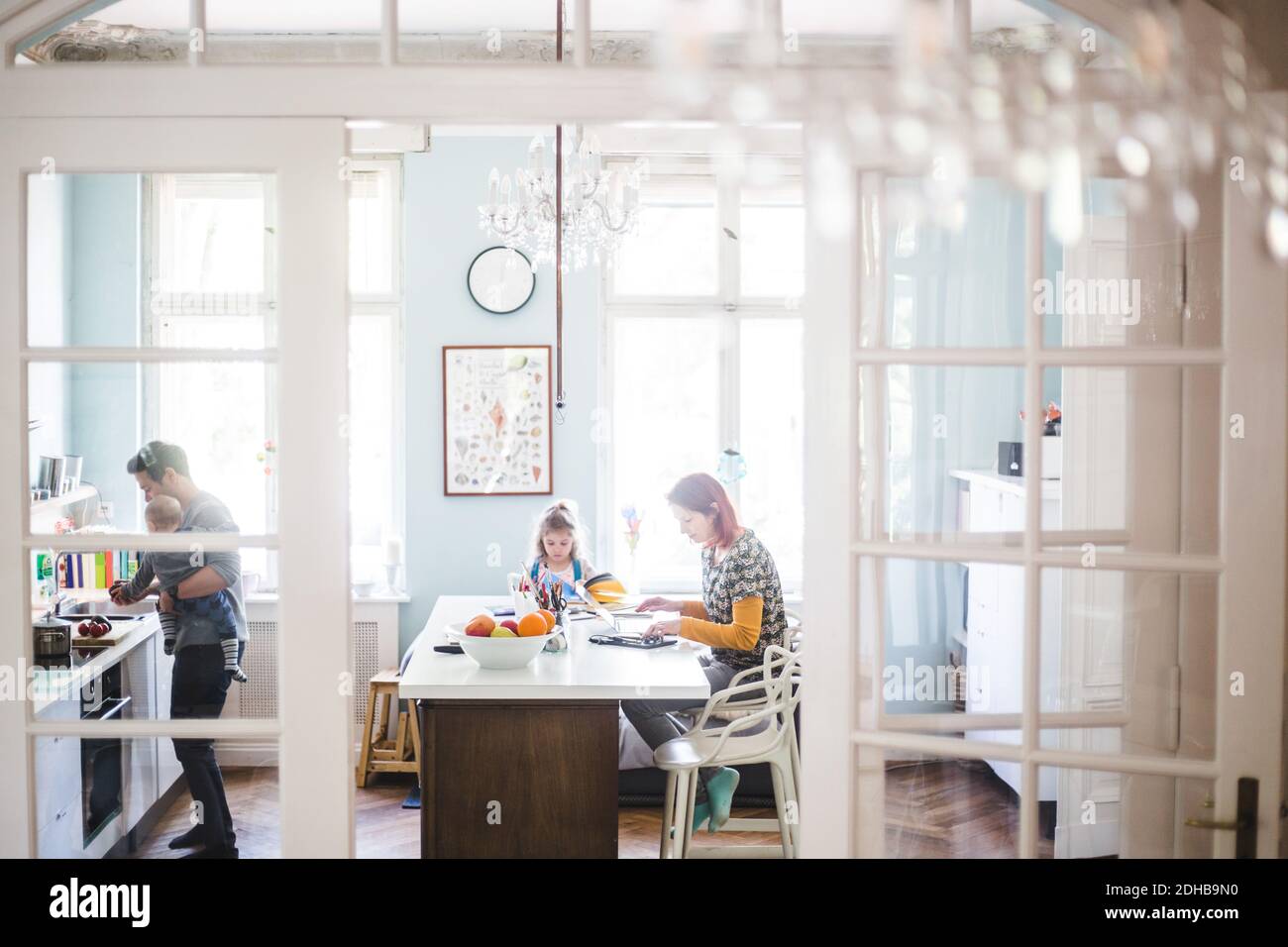Donna che usa il computer portatile mentre si siede con una ragazza che studia in cucina isola Foto Stock