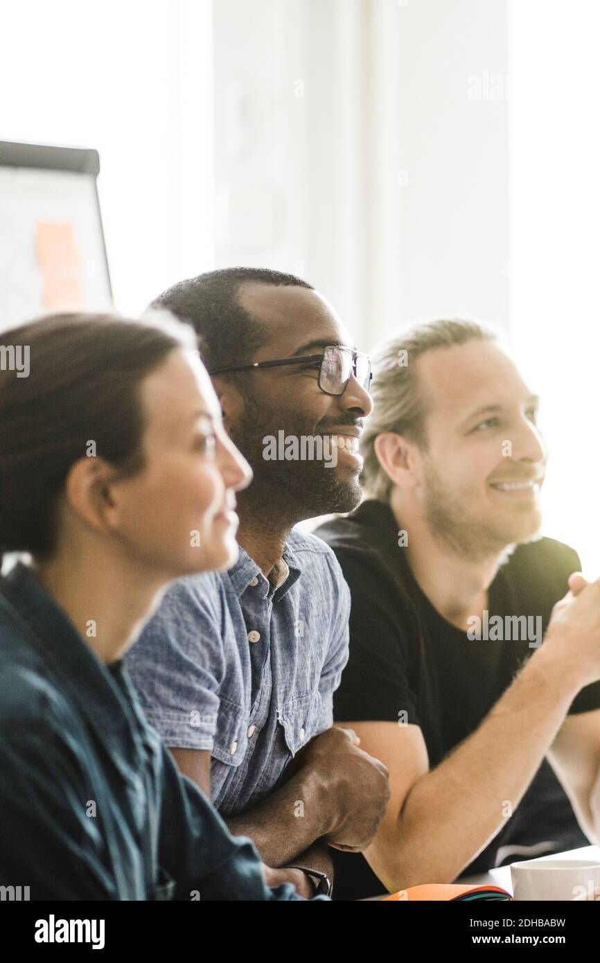 Sorridente uomini e donne di affari che ascoltano in riunione a. ufficio creativo Foto Stock