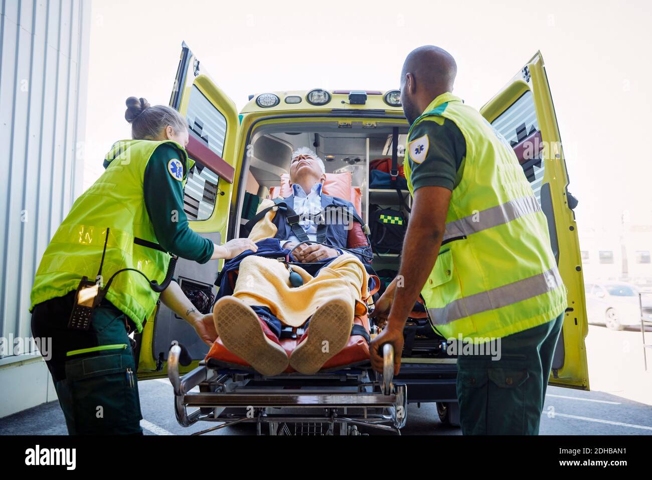 Paramedici che tirano l'uomo d'affari dall'ambulanza sul gurney dell'ospedale Foto Stock