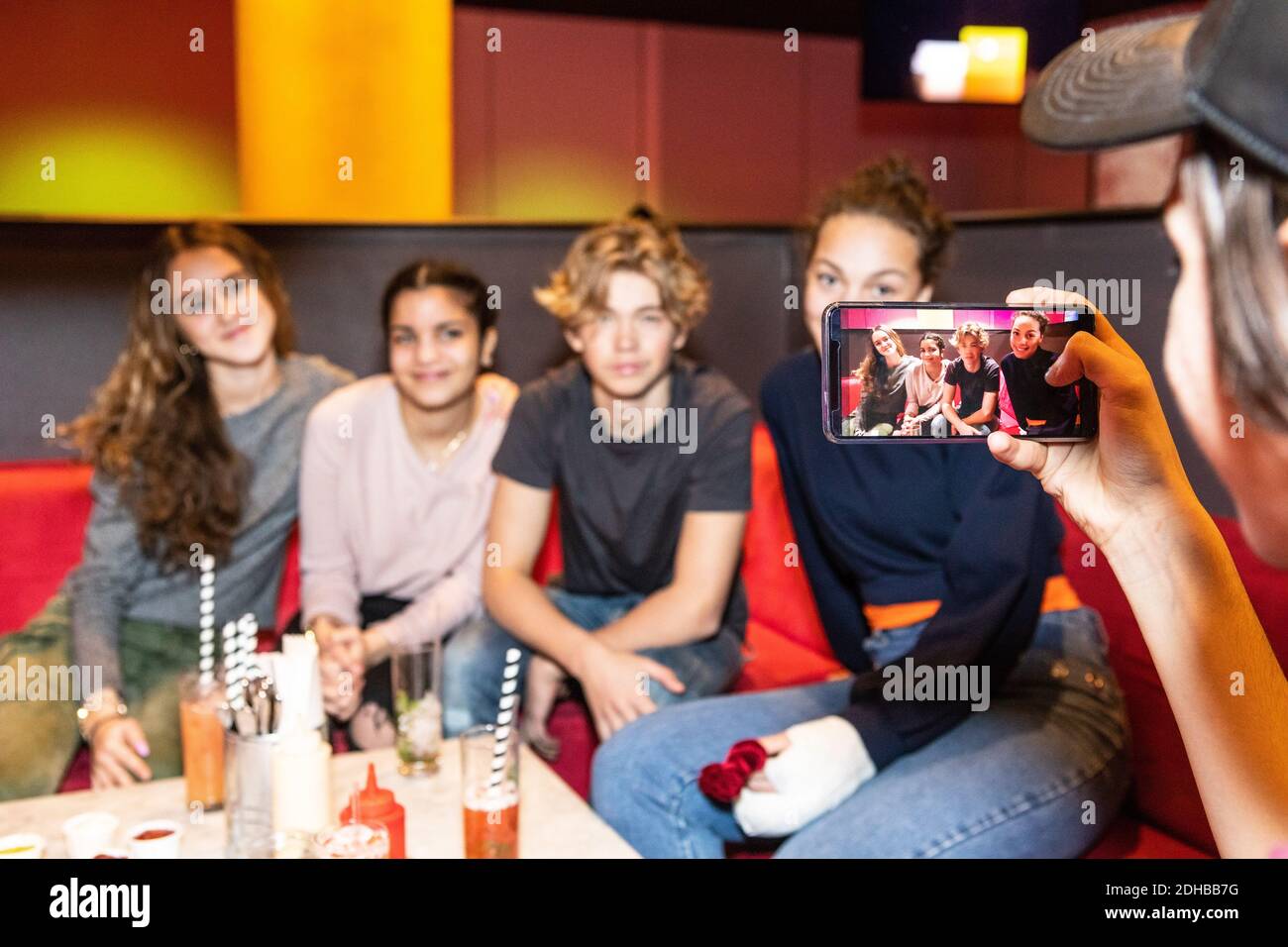 Immagine ritagliata di un ragazzo adolescente che fotografa amici multietnici seduti divano al ristorante Foto Stock