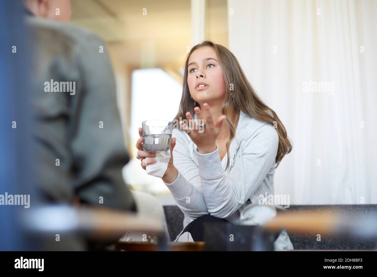 Adolescente depresso che parla con il terapeuta mentre beve acqua in officina Foto Stock