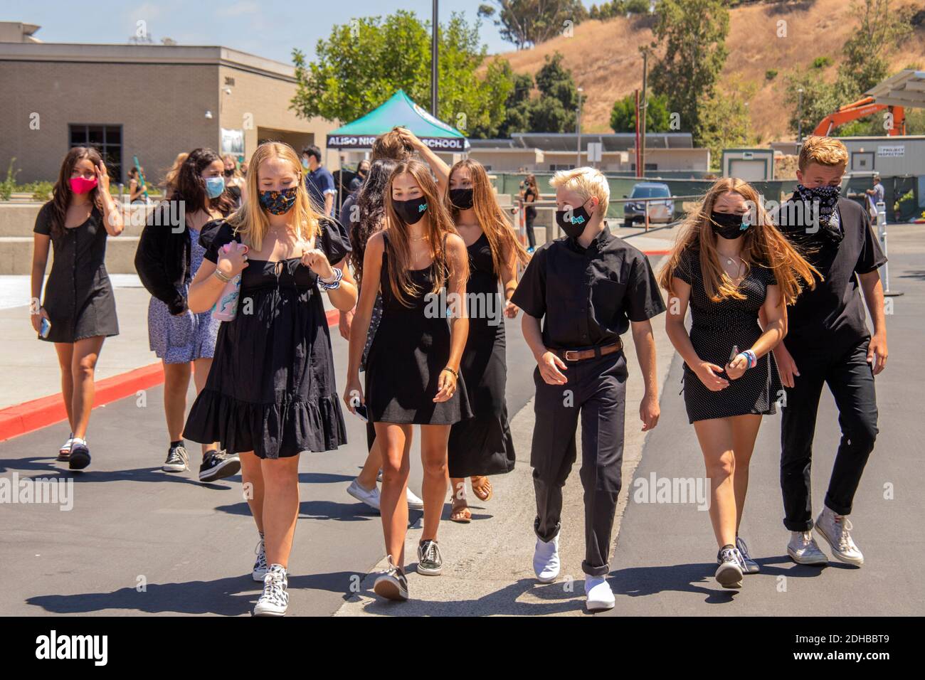 Vestiti in nero cerimoniale e indossando maschere per il viso a causa della pandemia del coronavirus, gli studenti di una scuola superiore della California meridionale arrivano per assistere WIT Foto Stock