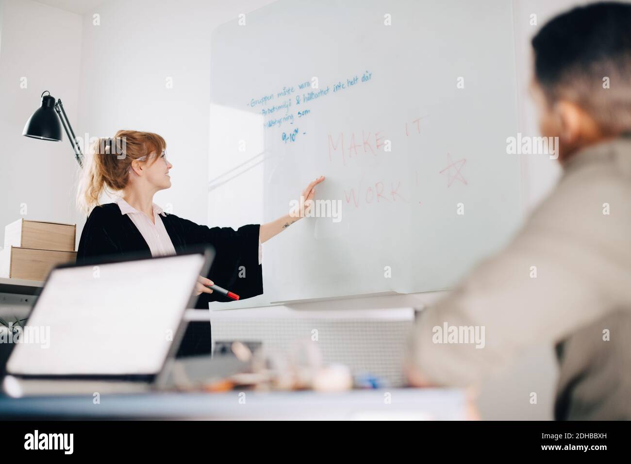 Vista ad angolo basso di una giovane donna d'affari in piedi in vetro acrilico con un collega in sala riunioni in ufficio Foto Stock