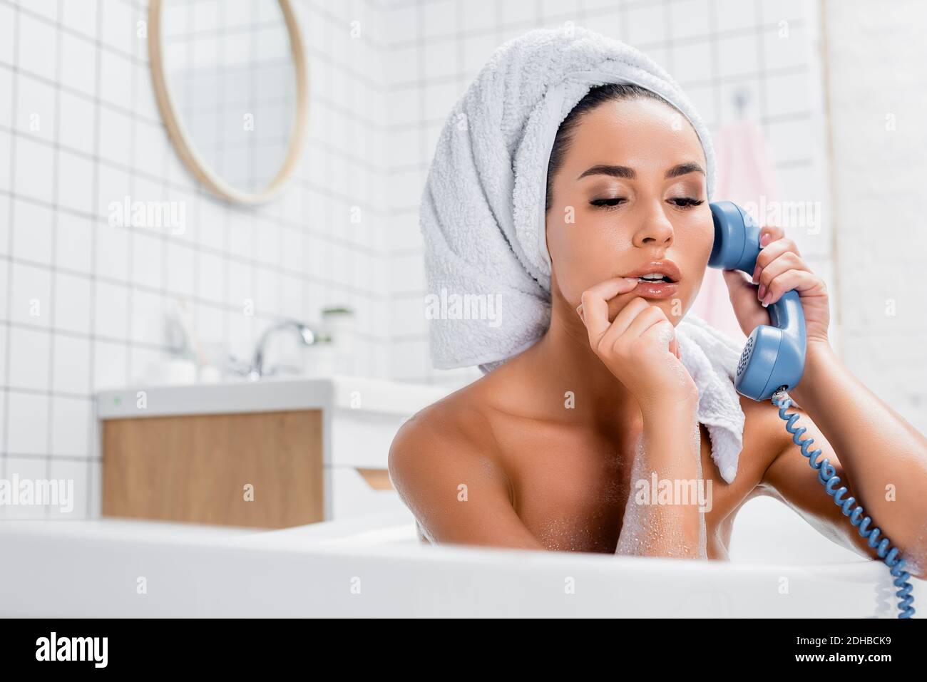 Giovane donna con asciugamano sulla testa e dito vicino alle labbra parlare  al telefono in bagno in primo piano sfocato Foto stock - Alamy