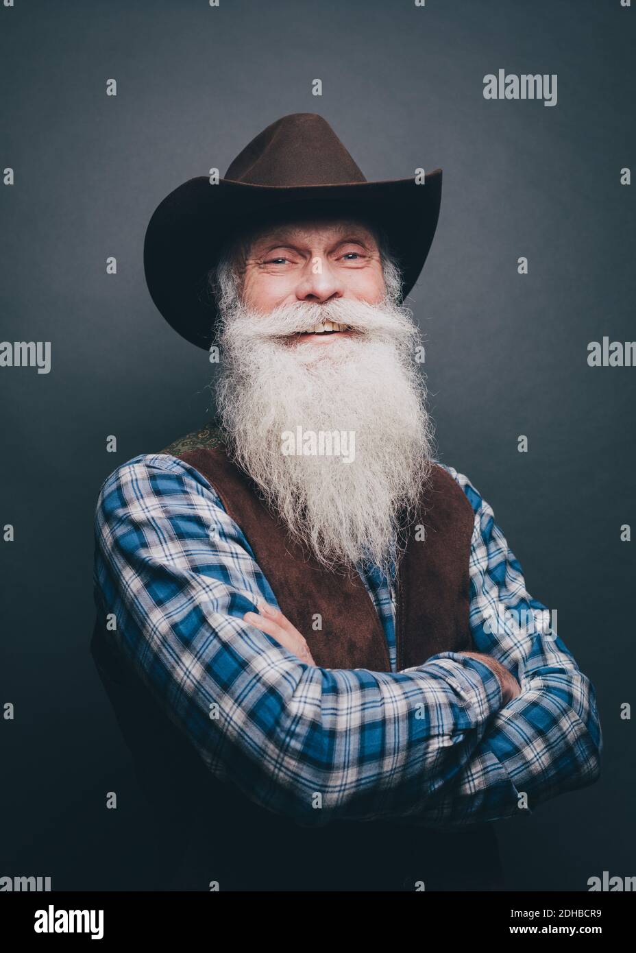 Ritratto dell'uomo anziano felice che indossa cappello da cowboy contro il grigio sfondo Foto Stock