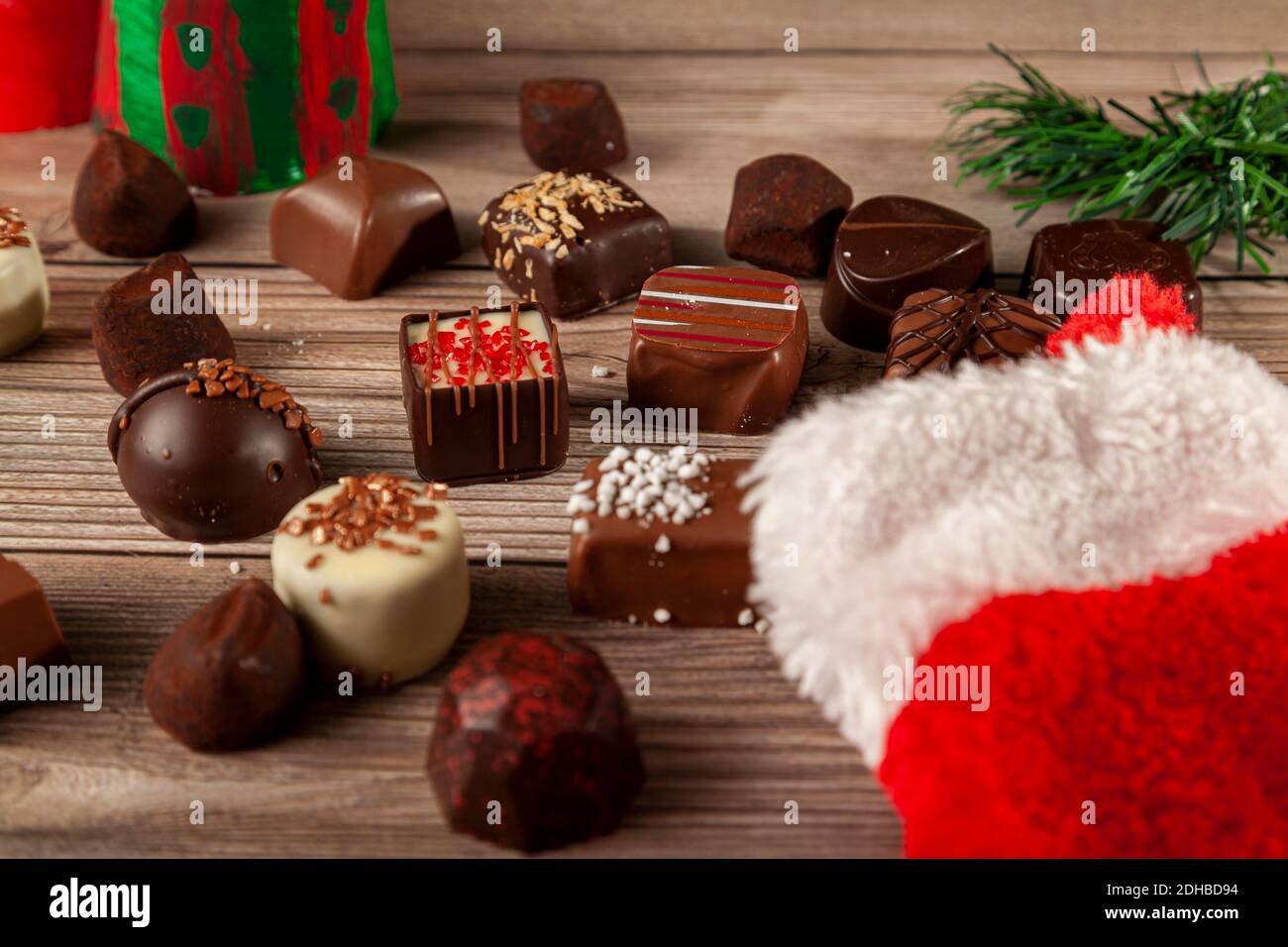 Pezzi di deliziosi cioccolatini assortiti stanno uscendo da una calza natalizia su un tavolo di legno. Pino albero di natale pezzo con l'arredamento regalo di vacanza sono Foto Stock