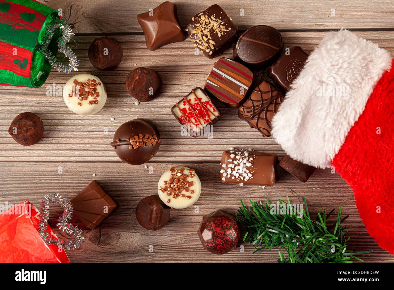 Pezzi di deliziosi cioccolatini assortiti stanno uscendo da una calza natalizia su un tavolo di legno. Pino albero di natale pezzo con l'arredamento regalo di vacanza sono Foto Stock