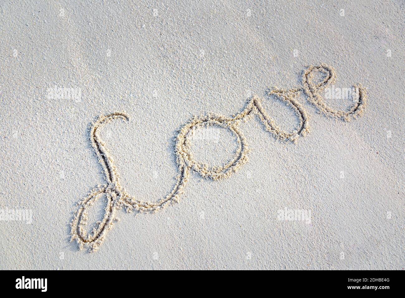 Mano che scrive amore sulla sabbia con spazio di copia. Romantico modello di spiaggia, parola d'amore su sfondo di sabbia, look 3D. Foto Stock