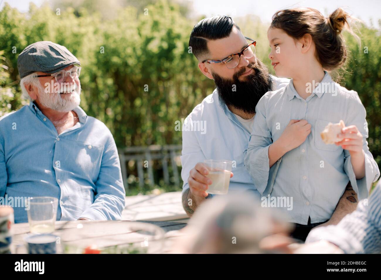 Uomo anziano sorridente che guarda la famiglia avendo cibo nel patio Foto Stock